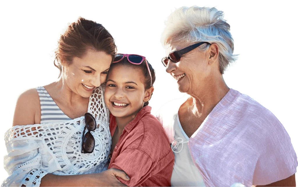 Three women from different generations—an elderly woman in glasses, a middle-aged woman, and a young girl—smile together. They appear happy and are dressed casually, with the middle-aged woman and the girl sharing a warm embrace.